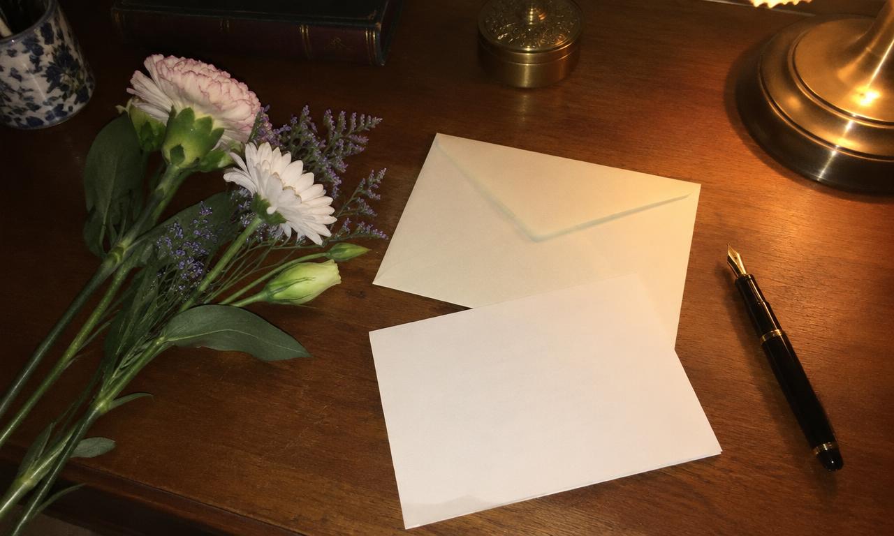 Une enveloppe, une plume et quelques fleurs posées sur un bureau de soirée.